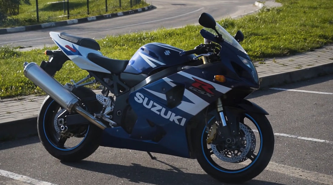 blue Suzuki bike in parking, road behind, and grass