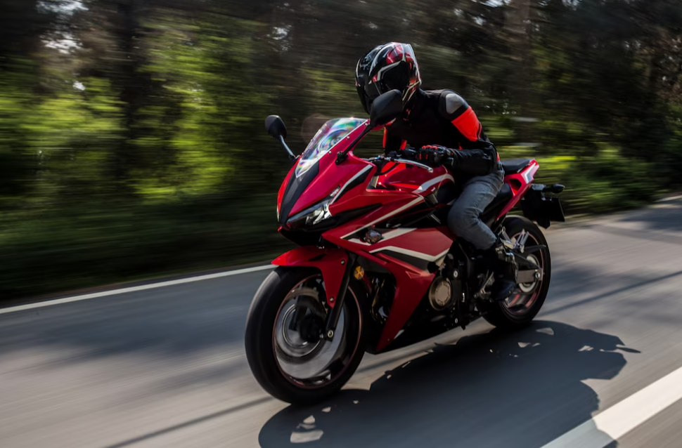 man riding fast on his red bike on the road, forest near the road